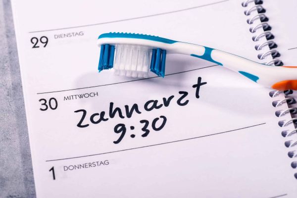 Regelmäßige Termine in der Zahnarztpraxis auf einem Kalenderblatt mit Zahnbürste.